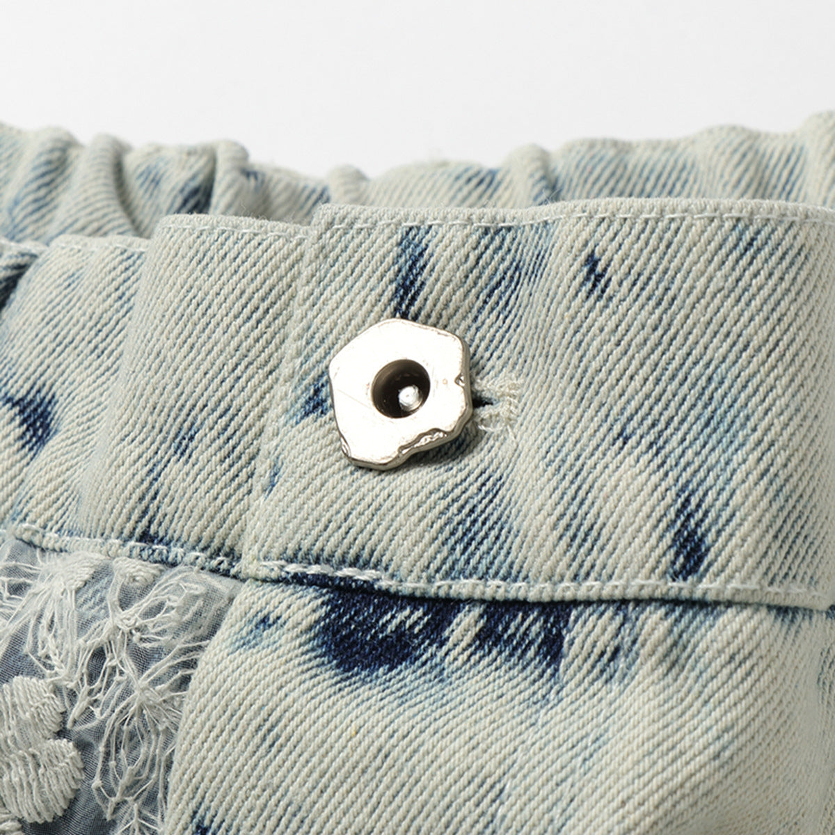 Close-up of the metal button and waistband on pale blue acid-wash denim shorts.
