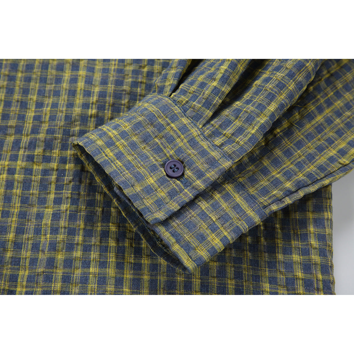 Close-up of the plaid shirt's long sleeve cuff and dark button against the blue-gray and mustard check pattern.