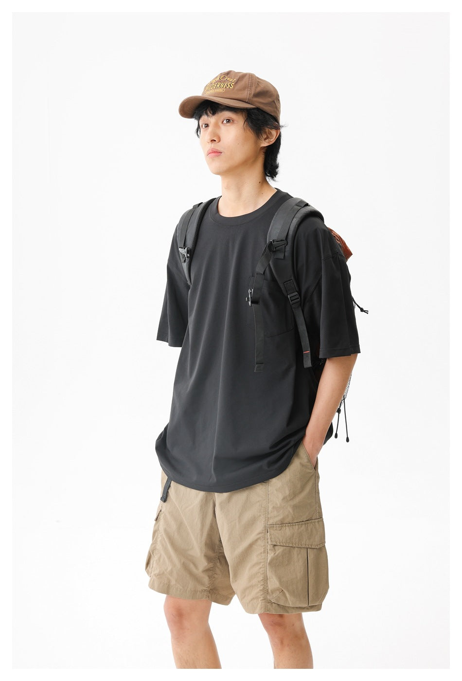 Closer view of a model wearing a black pocket T-shirt and tan cargo shorts with a backpack.