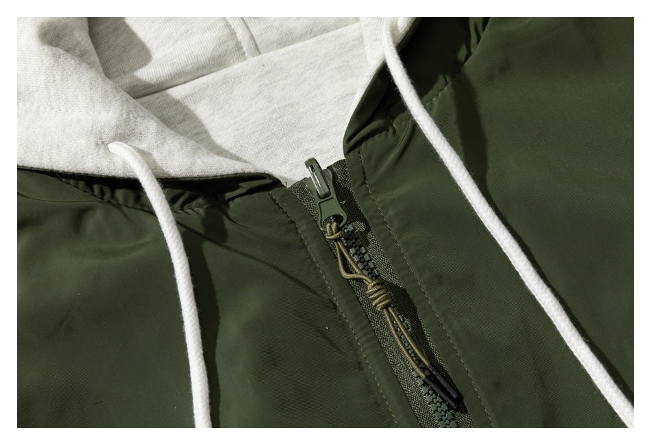 Close-up of a dark olive jacket zipper with a cord pull, white drawstrings, and light gray hood lining.