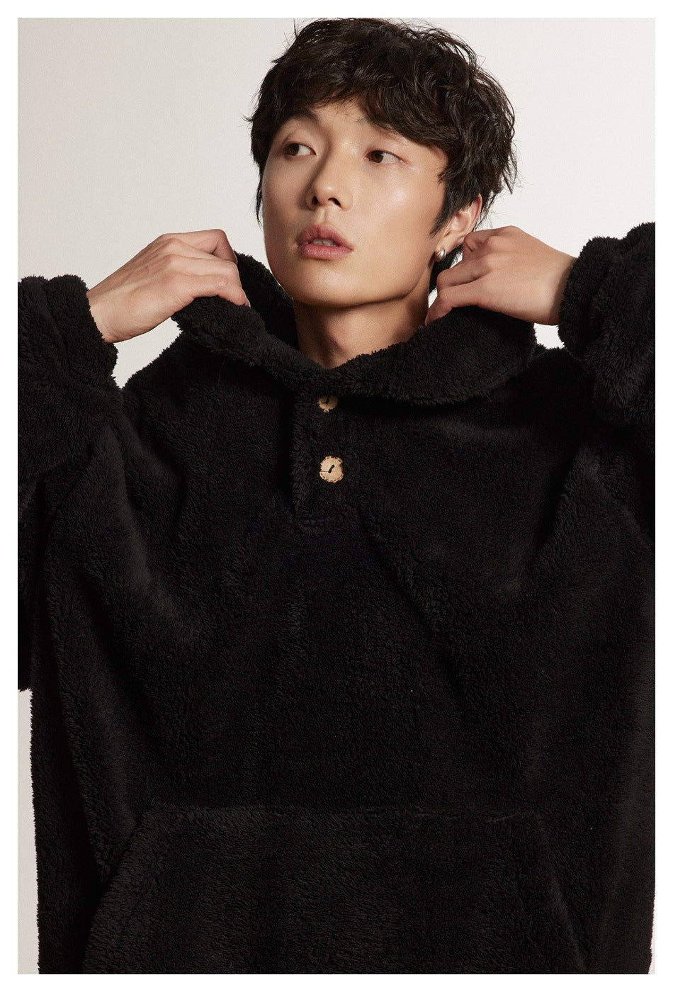 Close-up of a black plush pullover's wide collar, two wooden-look buttons, and front pocket.