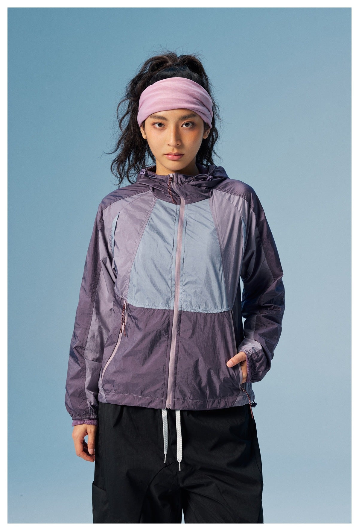 Front view of a model wearing a purple and pale blue color-block hooded jacket with a front zipper and drawcord details.