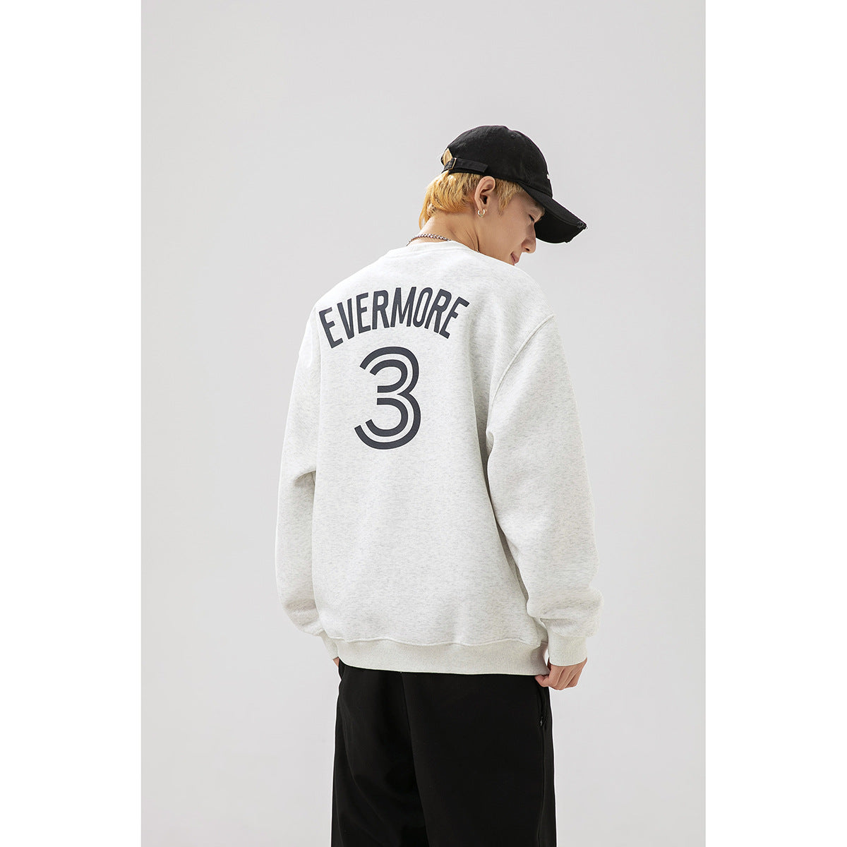Back view of a model wearing a light gray sweatshirt with dark EVERMORE lettering and a large number 3.