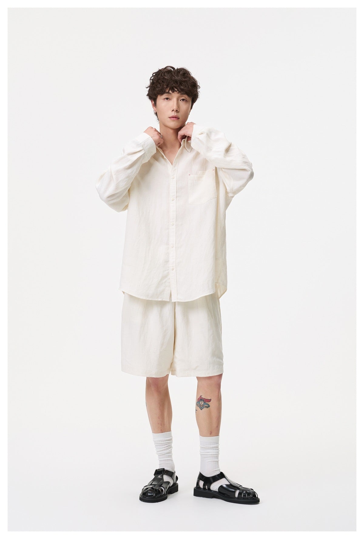 A man models an off-white button-up shirt with a chest pocket and matching shorts, shown from the front.