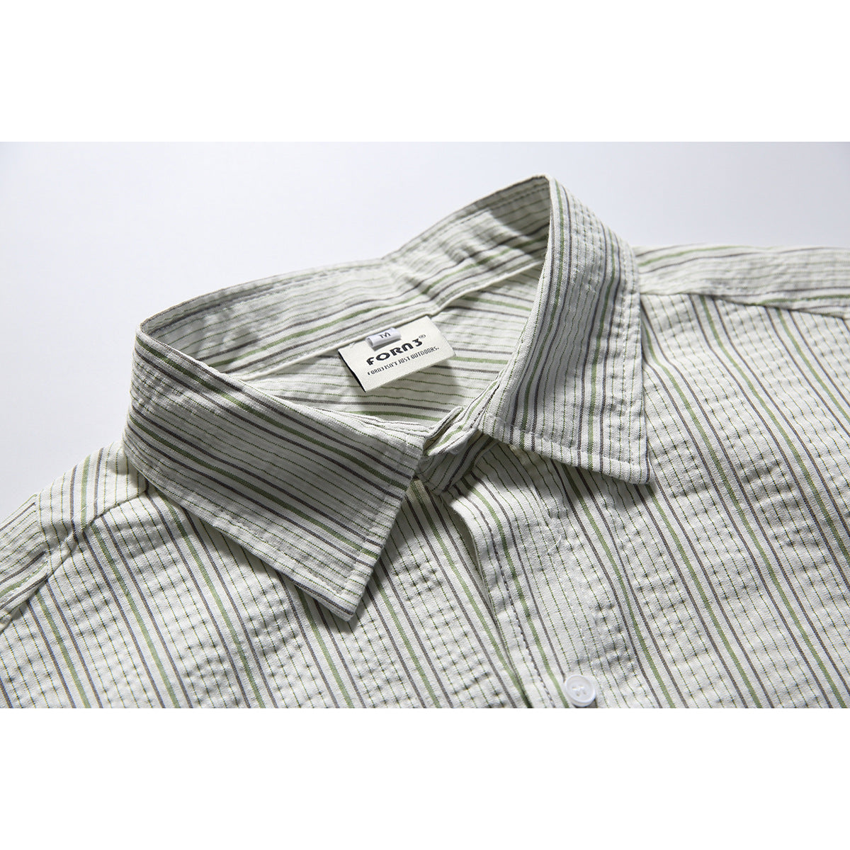 Close-up of a pointed collar on an off-white shirt with thin gray and muted green stripes and a visible neck label.
