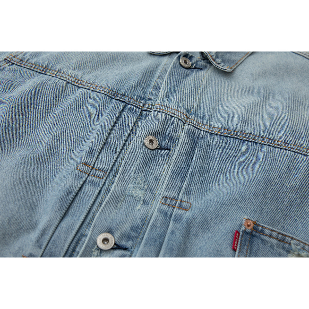Close-up of the light blue denim jacket front placket, metal buttons, seams, and distressed areas.