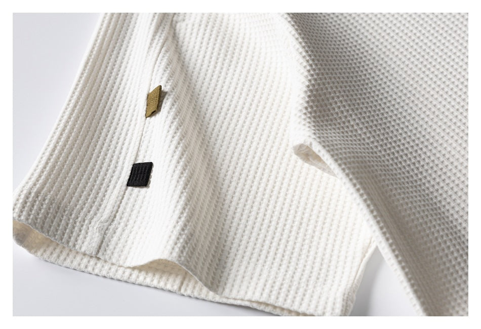 Close-up of ivory waffle-knit fabric and a seam with small tan and black fabric tabs.