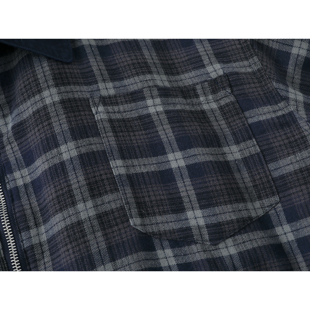 Close-up of a rectangular chest pocket on a dark blue and gray plaid jacket, with part of the zipper visible.