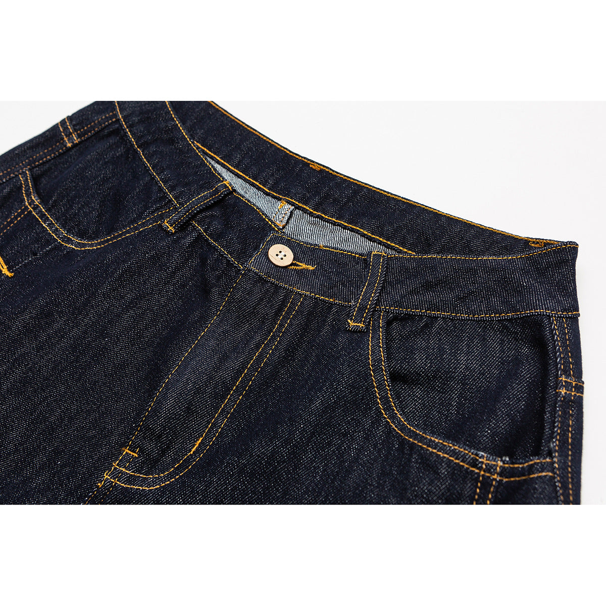Close-up of dark indigo jeans showing the waistband, button, front pockets and golden contrast stitching.