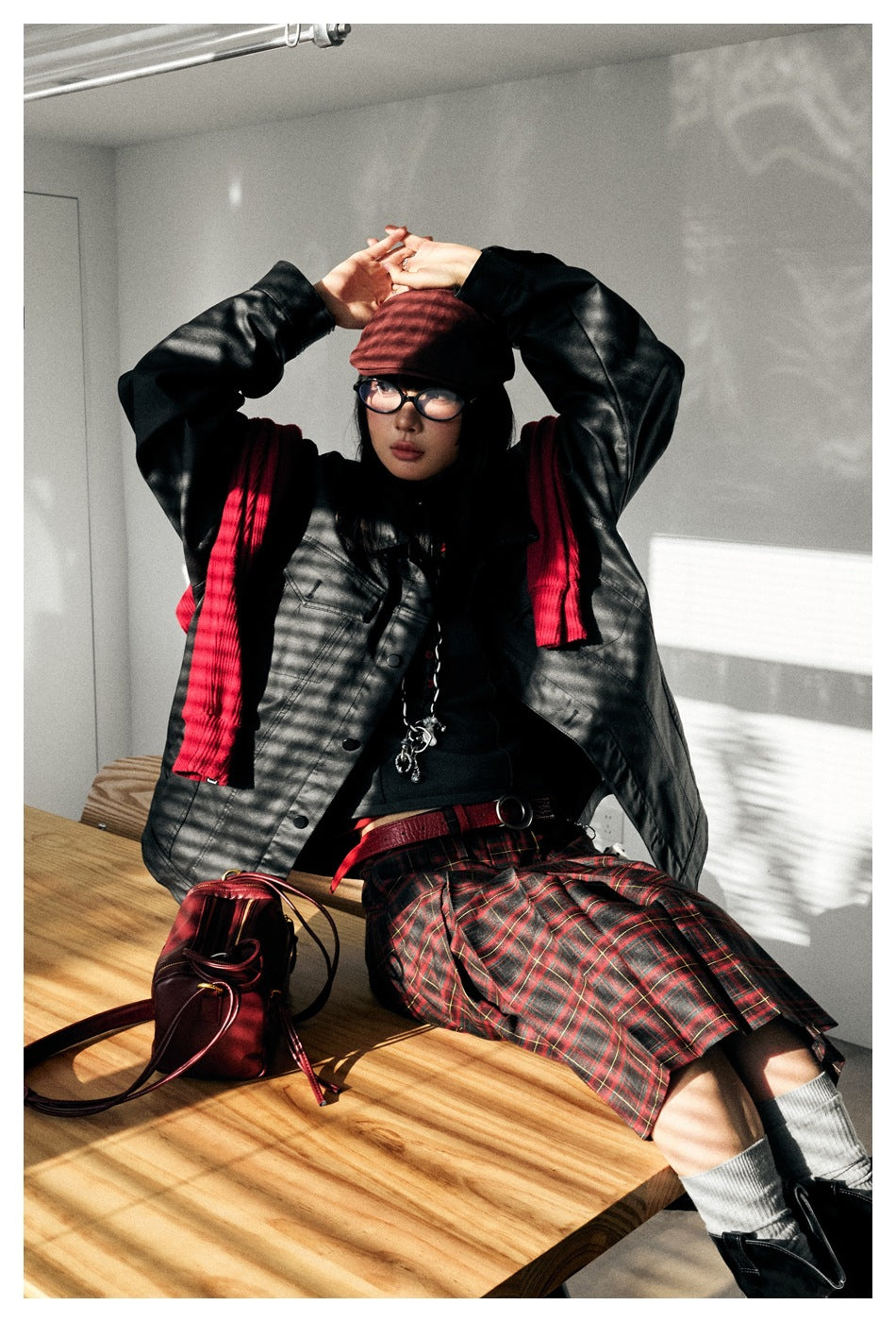 Model wearing an oversized black button-front jacket with a red scarf and plaid skirt.
