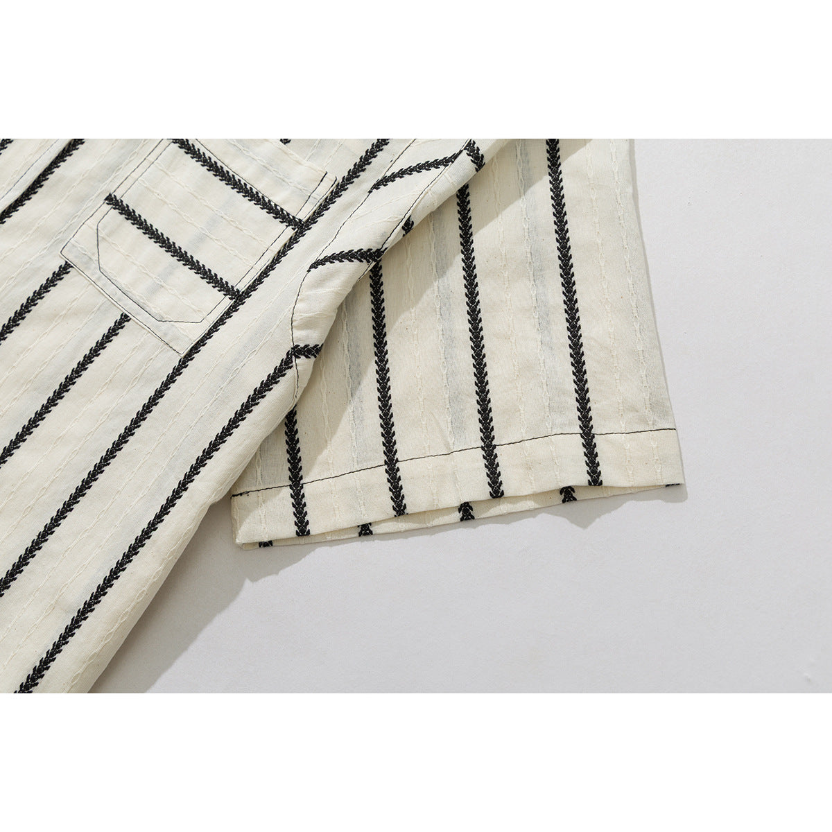 Close-up of the short sleeve hem and striped fabric of a cream shirt with black braided stripes.