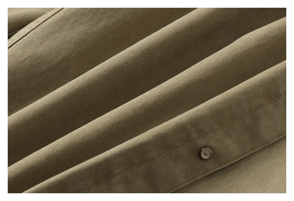 Close-up of khaki-brown garment fabric with diagonal folds, a stitched seam, and a small snap button.