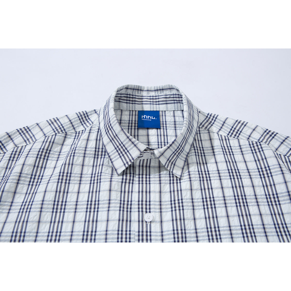 Close-up of a white button-up shirt collar with a blue-gray plaid pattern and a blue neck label.