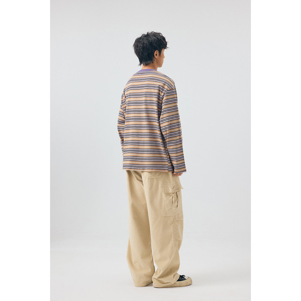 Rear three-quarter view of a model in a tan, navy and white striped long-sleeve shirt and beige cargo pants.