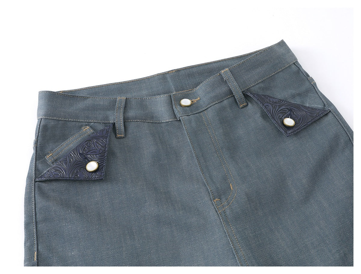 Close-up of blue-gray jeans showing the waistband, fly, and ornate dark pocket flaps with buttons.