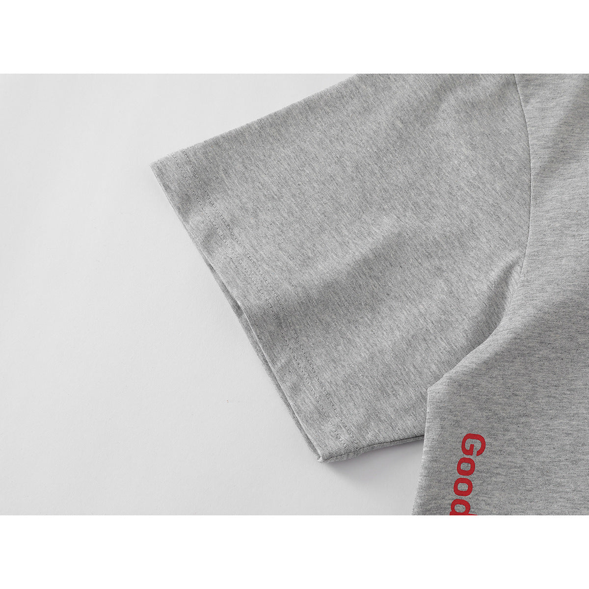 Close-up of a heather-gray T-shirt sleeve and seam, with part of a red English print visible.