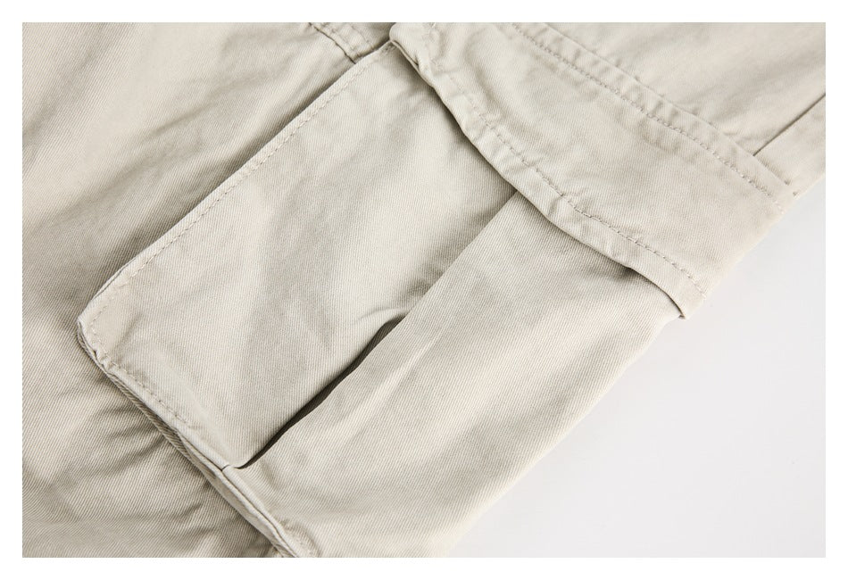 Close-up of light beige trousers showing a large rectangular pocket and stitched seams.