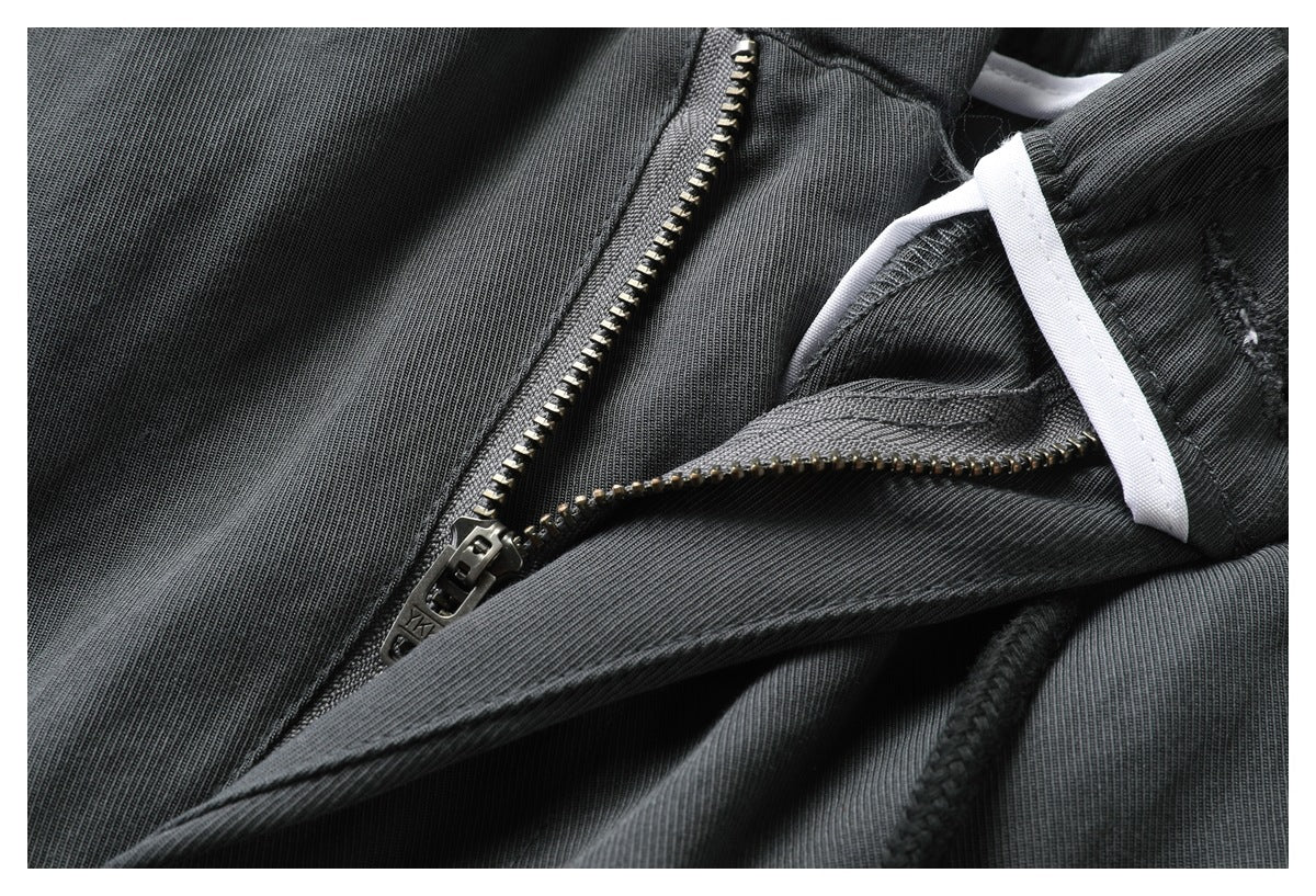 Close-up of charcoal trousers showing a metal zipper, seam details, and a white inner tie or trim.