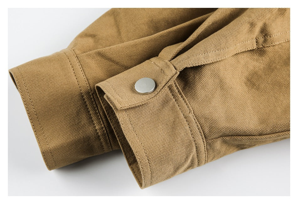 Close-up of a tan garment cuff with a silver snap and stitched fastening tab.
