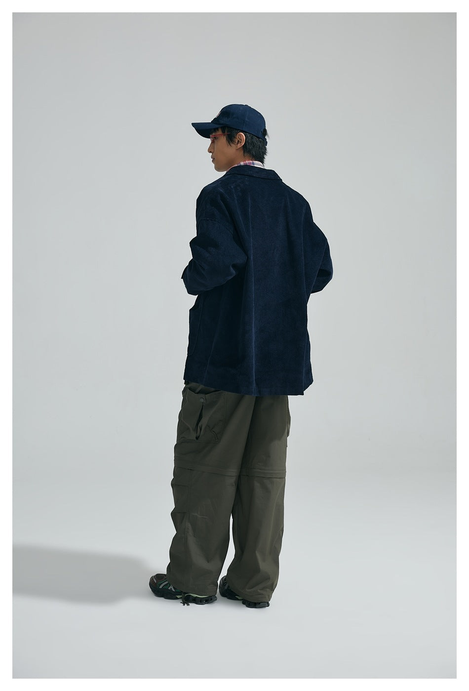 Back view of model wearing navy corduroy jacket with olive cargo pants and navy cap