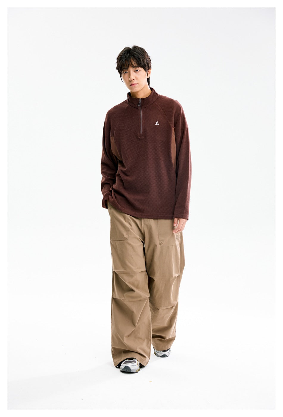 Model wearing a burgundy quarter-zip pullover with tan pants, standing in a front three-quarter pose.