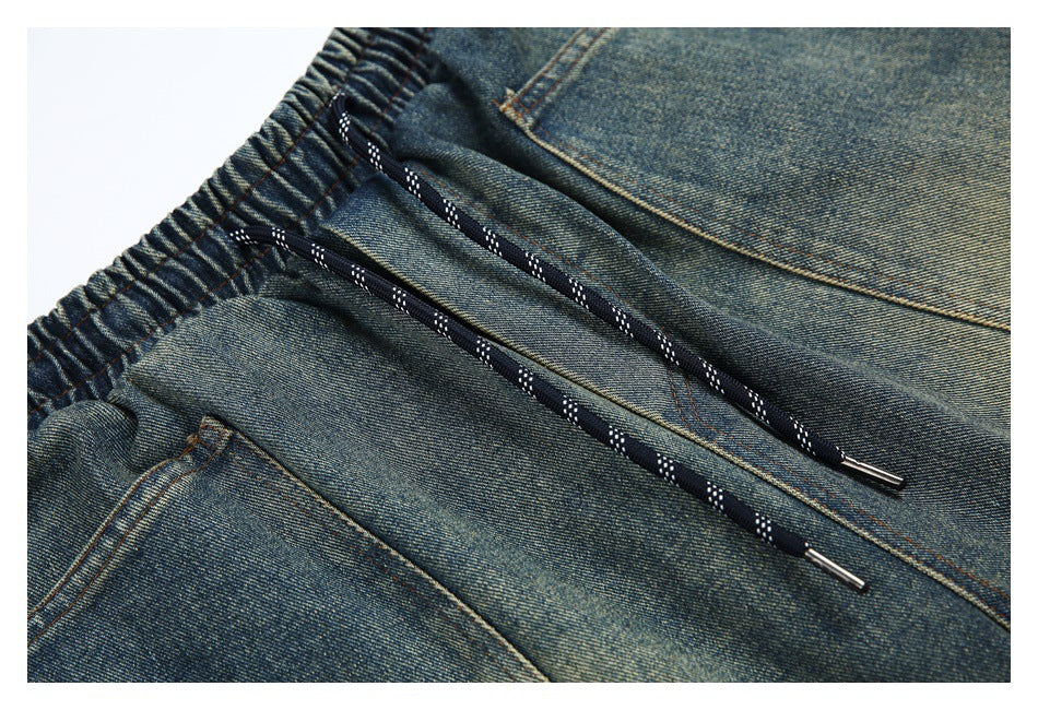 Close-up of faded blue denim shorts with a gathered waistband, black patterned drawcords, and pocket seams.