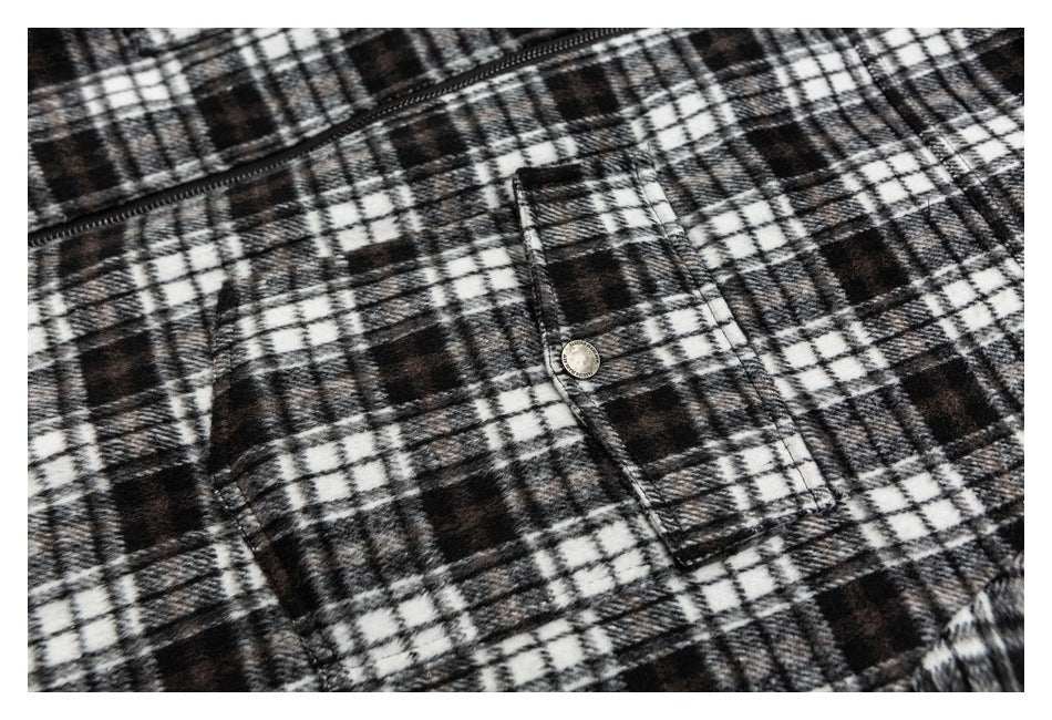 Close-up of a black-and-white plaid garment showing a zippered opening and a buttoned flap pocket.