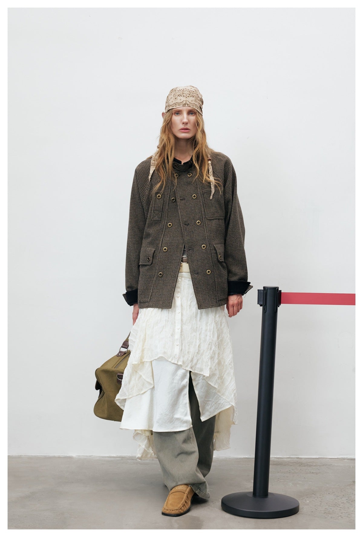 Full-length model wearing a dark brown checked double-breasted jacket over a layered white skirt and gray trousers.