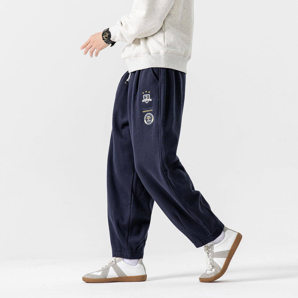 Side view of a model wearing navy relaxed joggers with a drawstring waist and embroidered thigh patches.