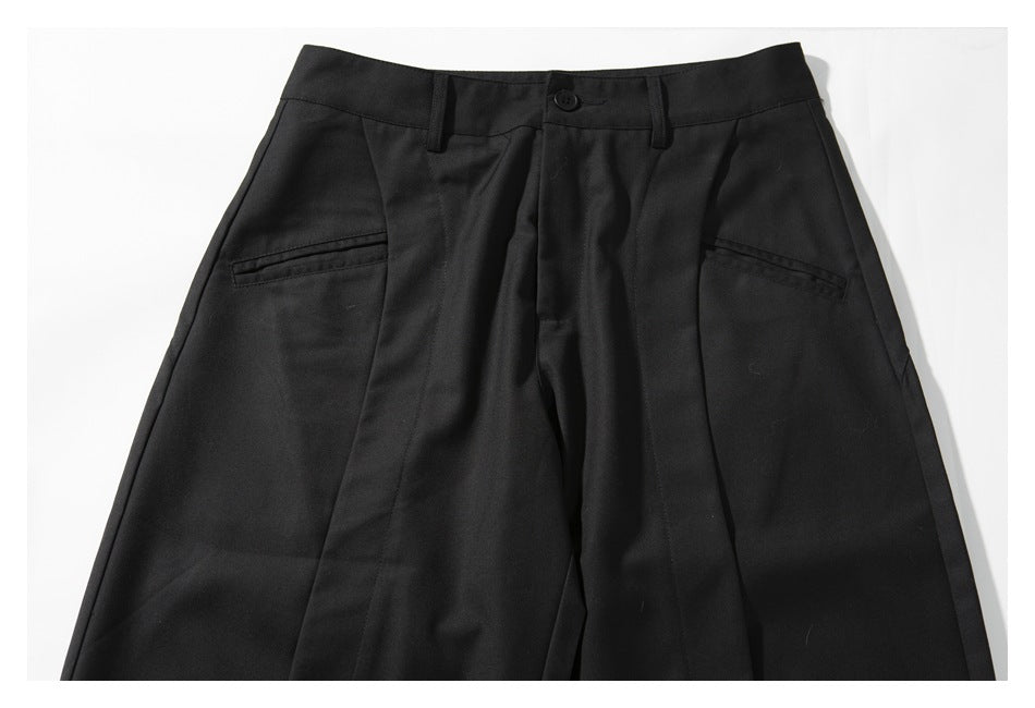 Upper front view of black trousers showing the waistband, button closure, pleats, and two pockets.
