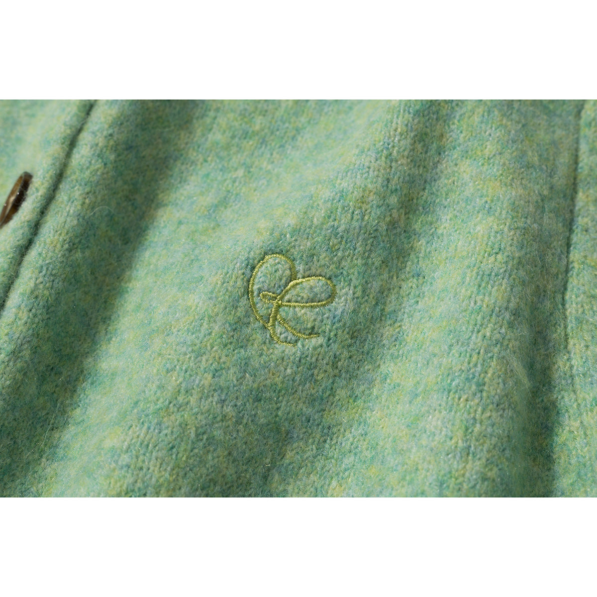 Close-up of a small embroidered motif on mottled mint green cardigan fabric.