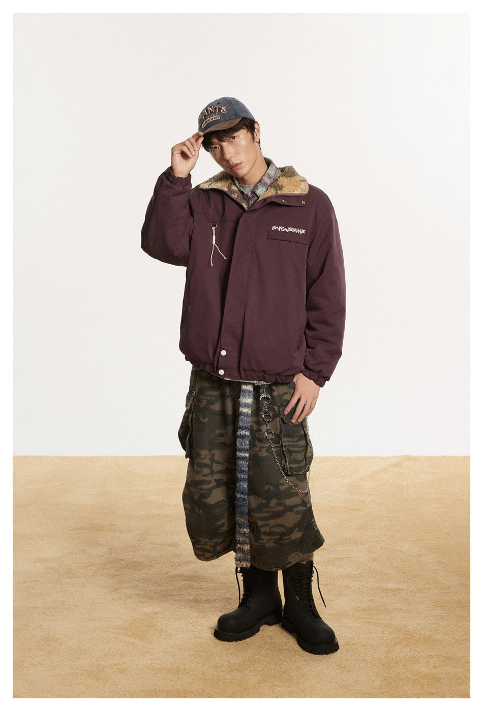 Model wearing a plum snap-front jacket with a fleece-lined collar, camouflage shorts, and black boots.