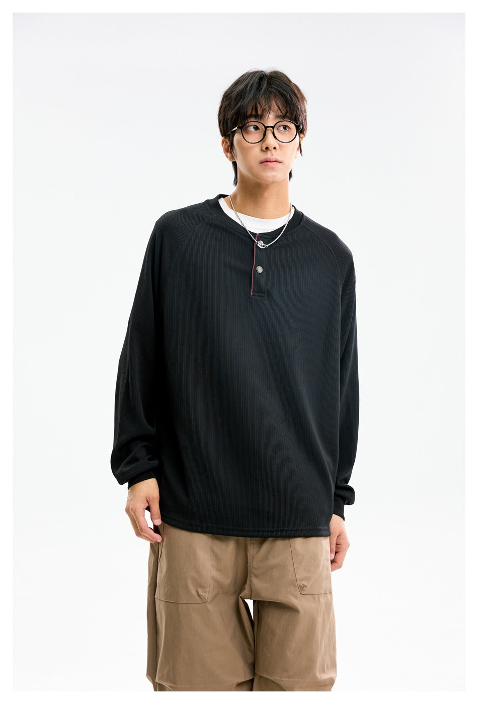 Model wearing a black ribbed long-sleeve henley with a short button placket and thin red trim.