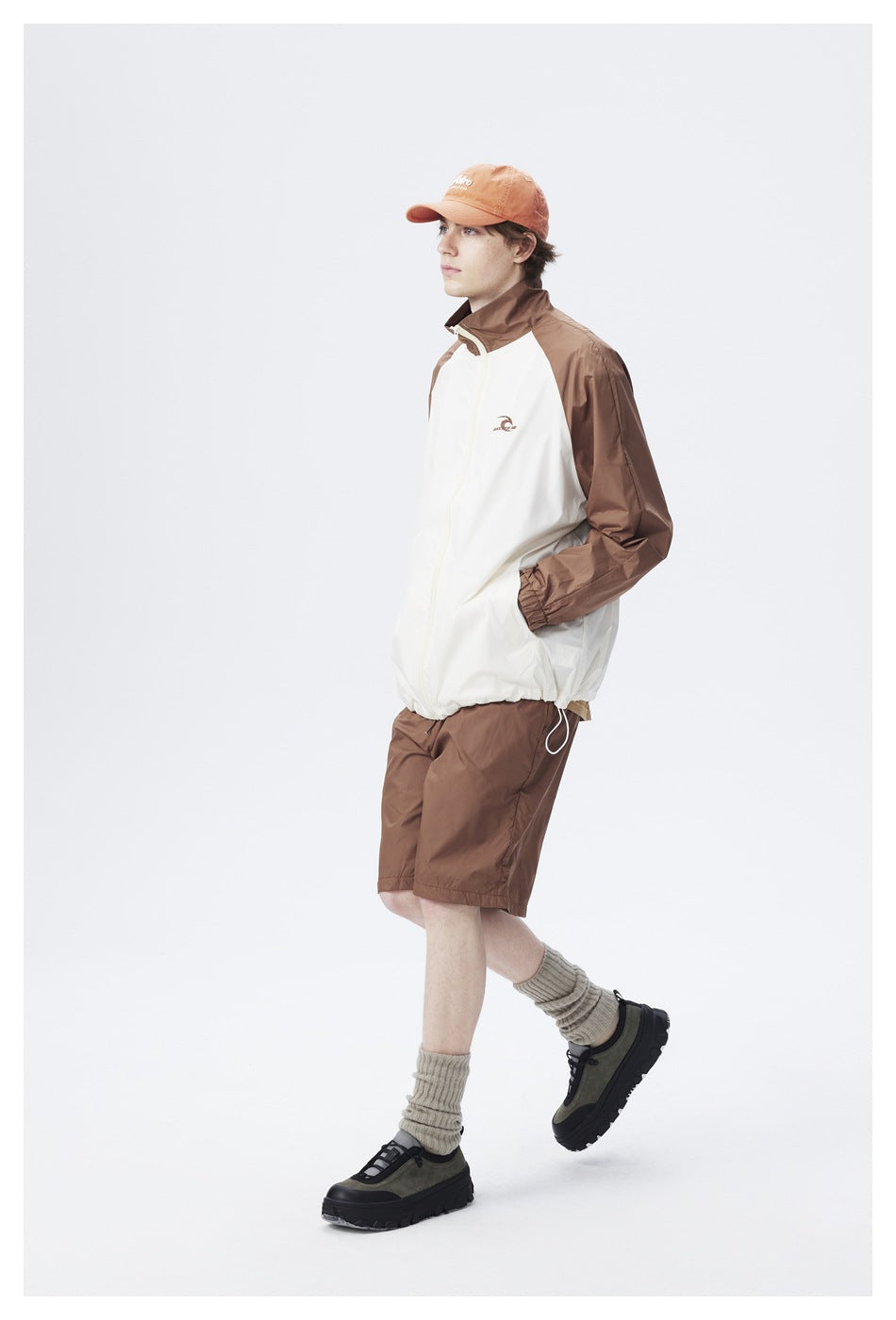 Side view of a model wearing a cream-and-brown color-block zip jacket and brown shorts.