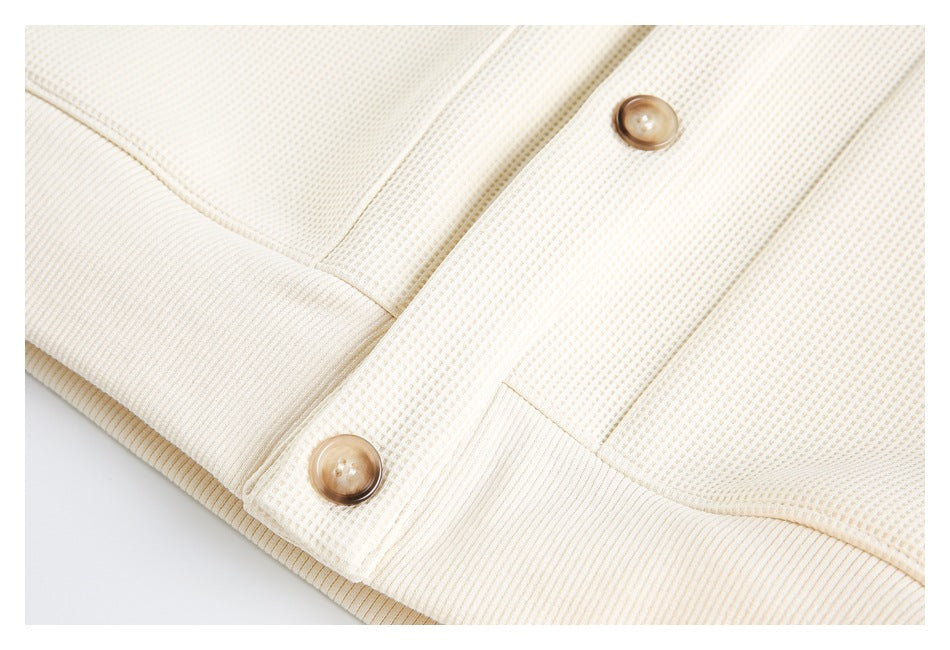 Close-up of the cream knit top's lower hem and button placket.