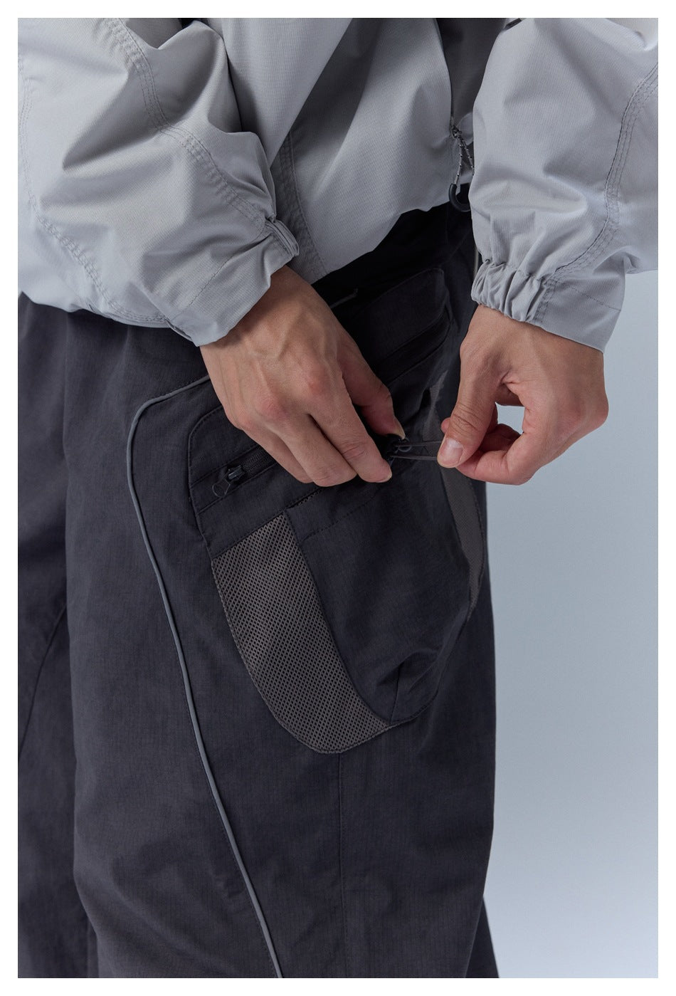 Close-up of a mesh-panel cargo pocket and drawcord on black pants.