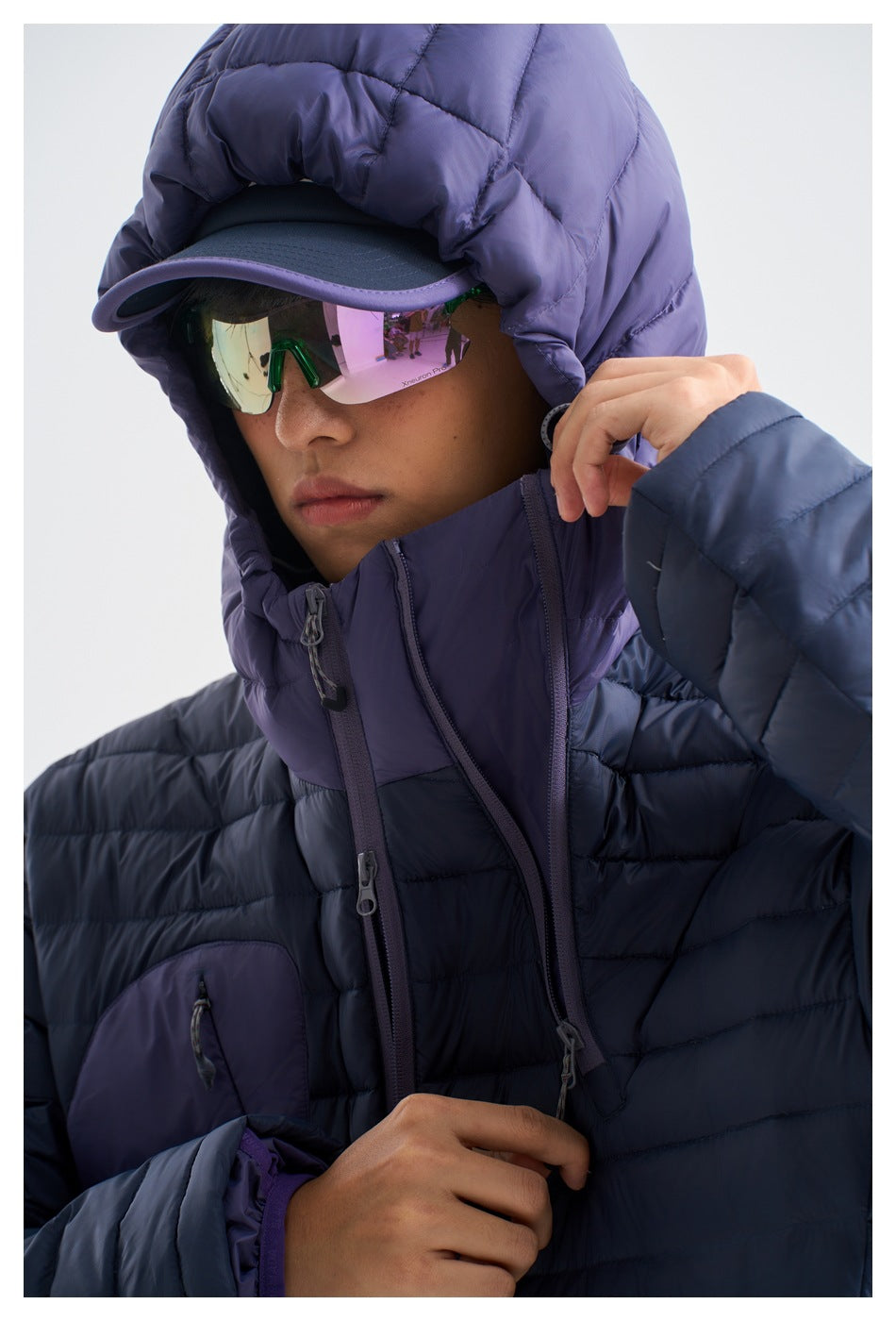 Close-up of a person wearing a navy quilted jacket with a purple hood and reflective sunglasses.