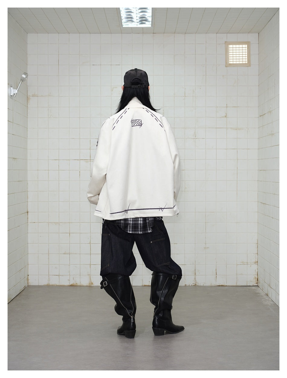 Rear view of a model wearing a cream jacket with black sketch graphics, dark jeans and tall black boots.