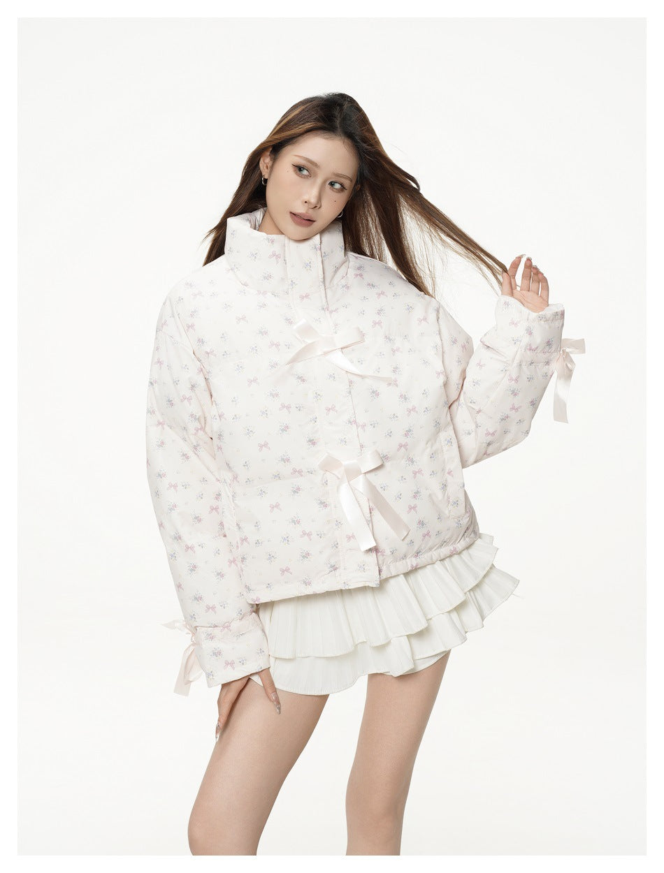 Model wearing a white high-collar jacket with a pastel bow-and-floral print and satin ribbon ties, shown from the front.