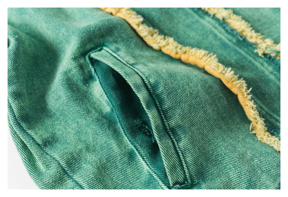 Close-up of a slanted pocket opening on teal denim, beside a yellow-frayed seam.
