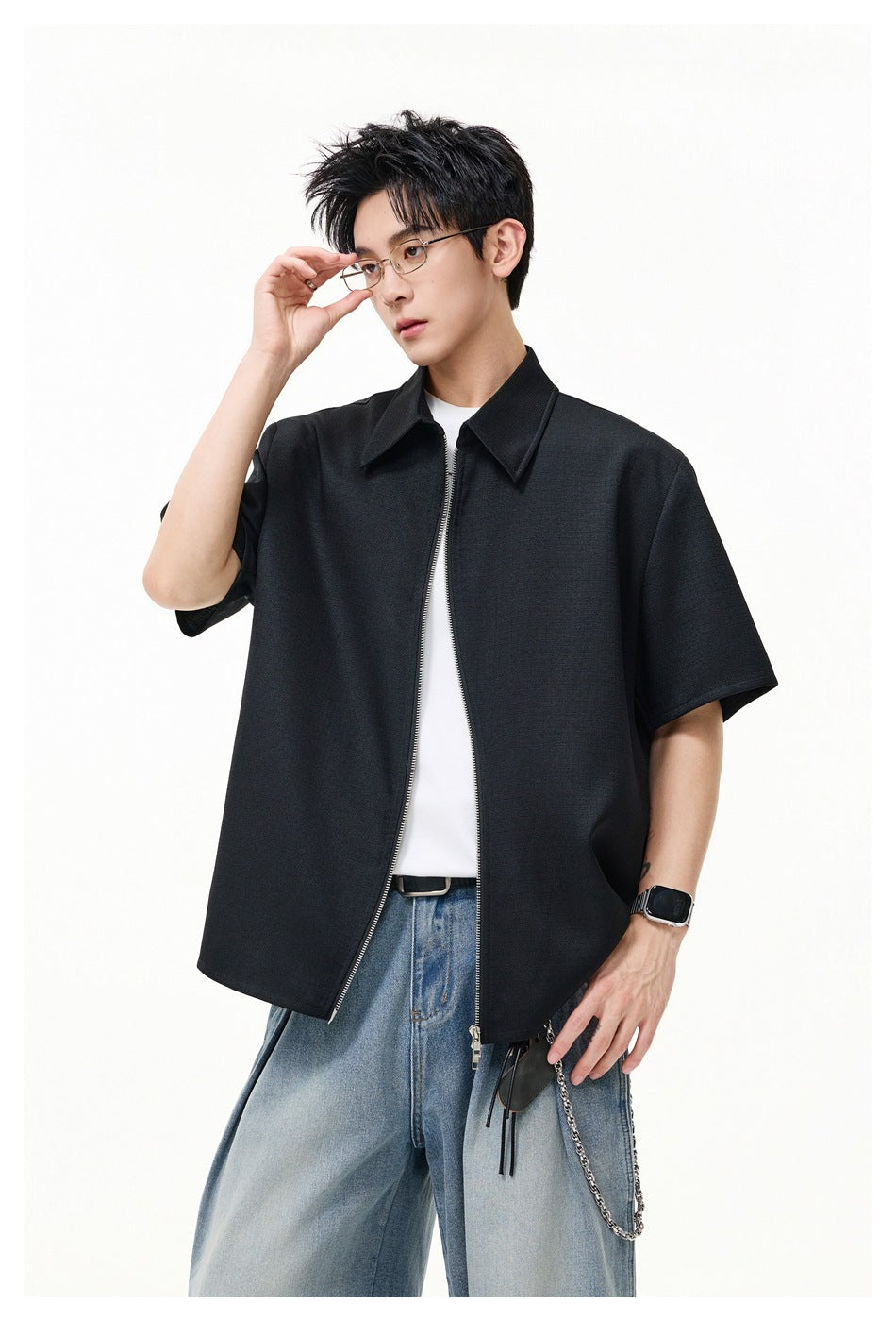 Model wearing a black short-sleeve collared zip-front shirt over a white tee with loose blue jeans.