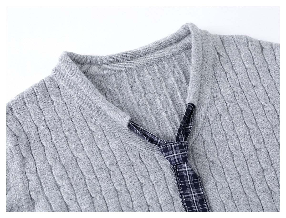 Close-up of the light gray cable-knit sweater neckline and its dark navy plaid tie detail.