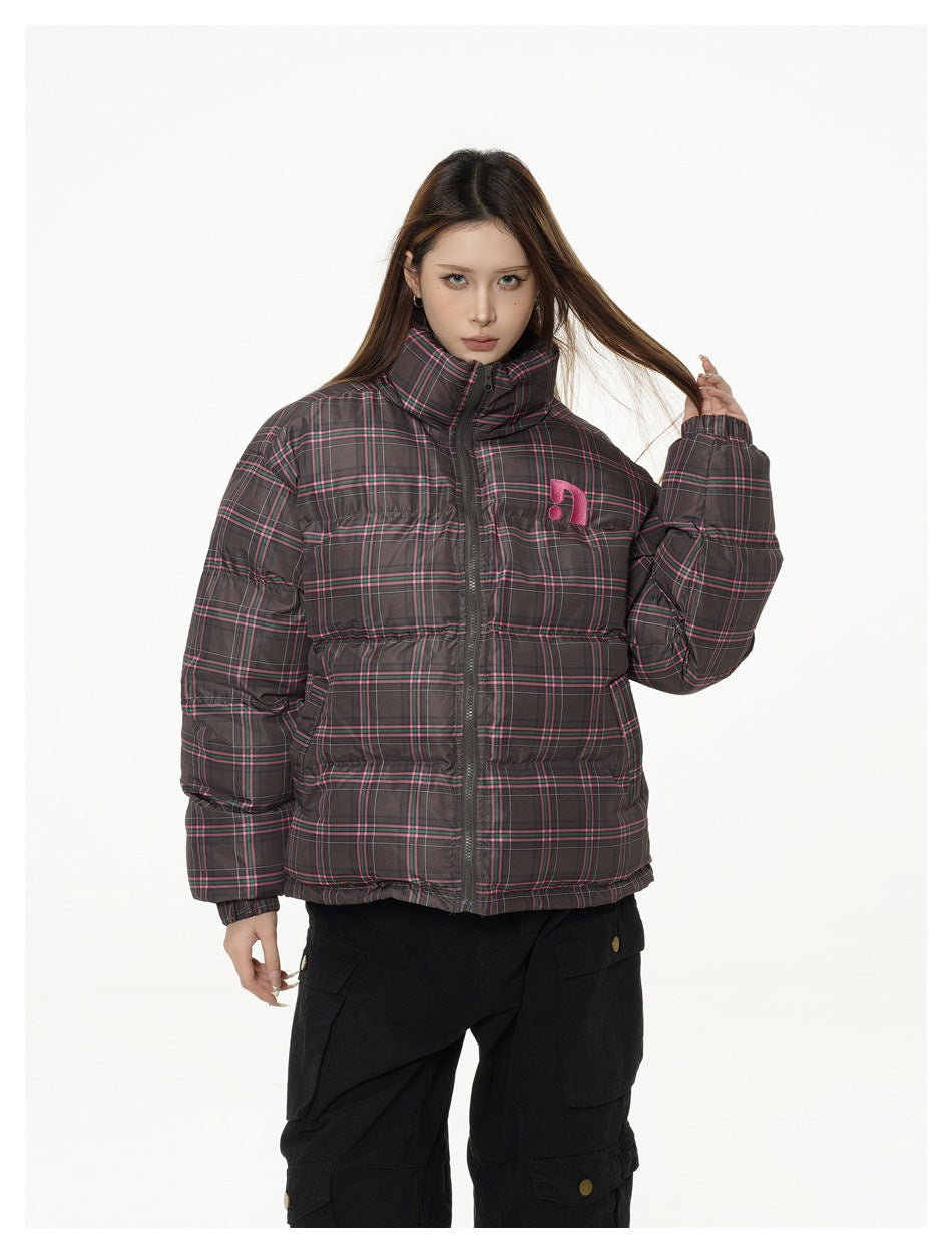 Woman wearing a brown plaid puffer jacket zipped up with black cargo pants, one hand touching her hair