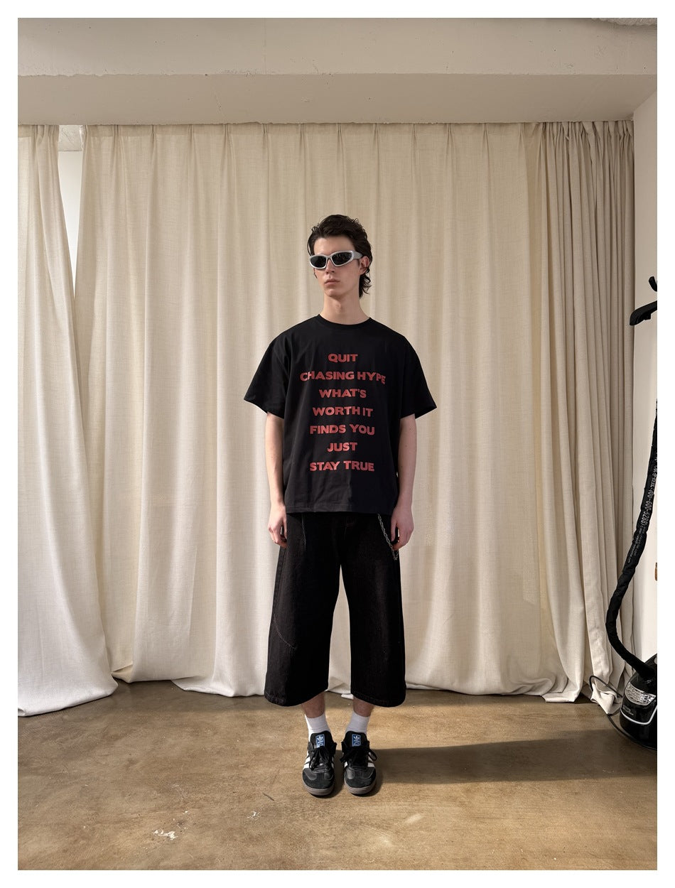 Full-length model wearing a black T-shirt with red text, black wide-leg shorts, and sunglasses.