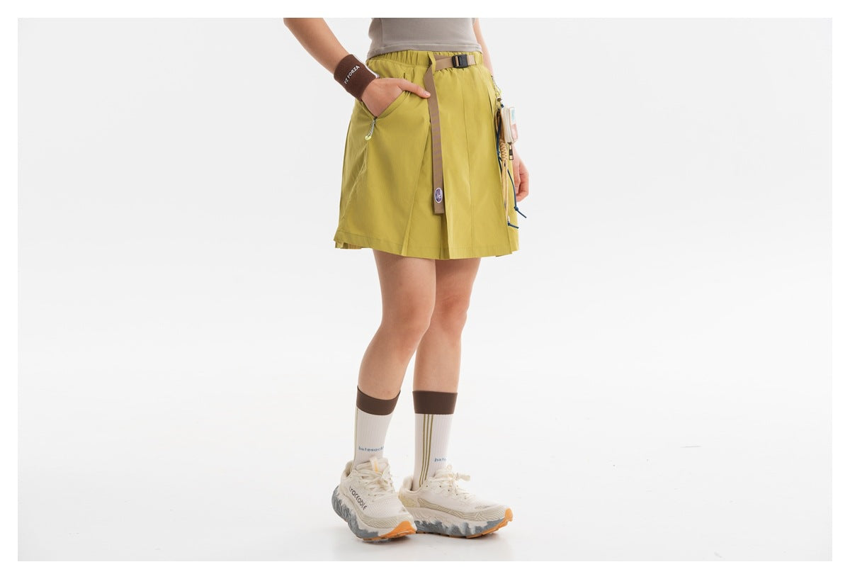 Cropped model wearing a chartreuse pleated skort with an elastic waist, belt, zip pockets and hanging strap.