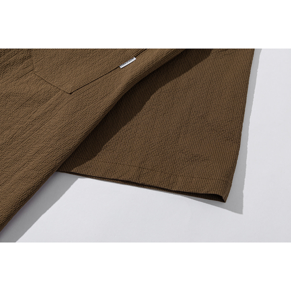 Close-up of a brown shirt showing a pocket edge, small sewn-in label and short-sleeve hem.