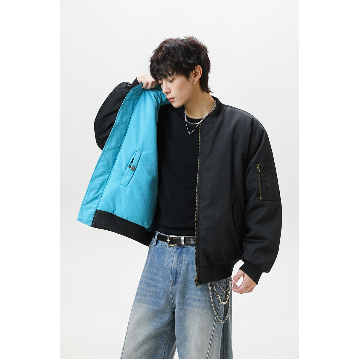 Model opens a black bomber jacket to show its bright turquoise lining, zip sleeve pocket, and ribbed cuffs.