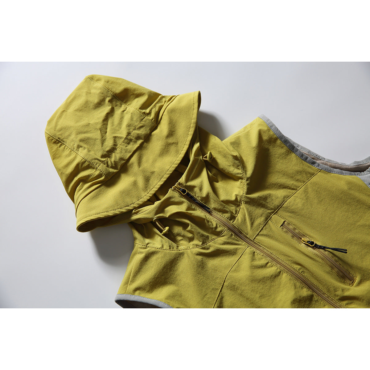 Close-up of a mustard yellow-green hooded vest with a front zipper, zip chest pocket, and gray mesh side panel.