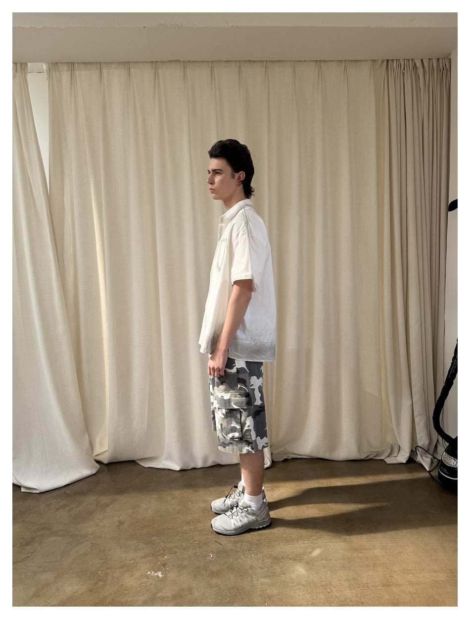 Full-length side profile of a model in a white short-sleeve shirt and gray camouflage cargo shorts.