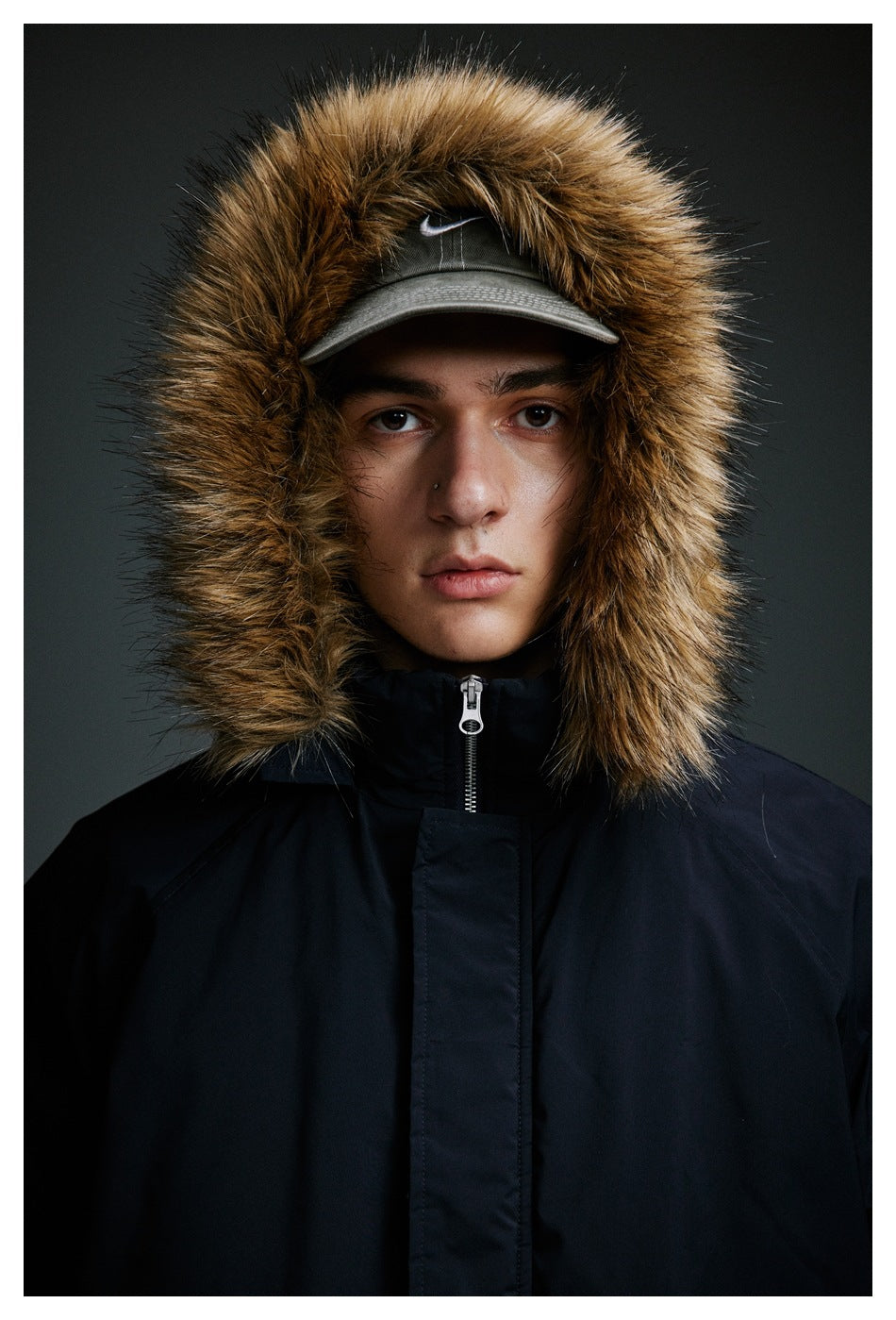 Close view of a model wearing a dark navy jacket with a tan fur-trimmed hood and high zipped collar.